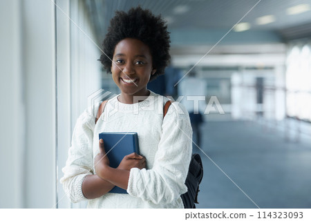 African girl, portrait and hallway of college with smile from happiness of education in academy. Student, learning and notebook on hand with information for class in school campus and scholarship African girl, portrait and hallway of college with smile from happiness of education in academy. Student, learning and notebook on hand with information for class in school campus and scholarship 114323093