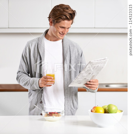 Breakfast, juice and man with newspaper in kitchen for information at modern apartment. Nutrition, cereal and young male person drinking healthy beverage and reading public journalism at home. 114323315