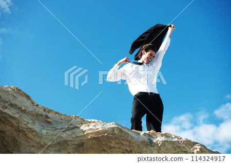 Cliff, business and man with celebration, excited and victory with holiday, smile and winning with promotion. Person, employee and consultant outdoor, nature and vacation with achievement or travel 114324917