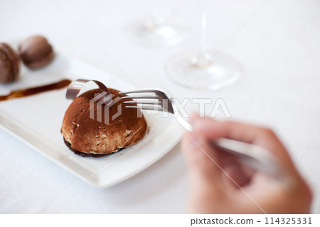 Hand, fork and eating chocolate dessert at restaurant, fine dining and food at cafe table. Closeup, mousse cake on plate and person hungry for luxury breakfast meal, cacao sugar or sweets in bakery 114325331