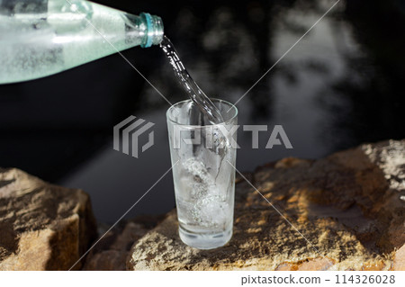 cold mineral water from a bottle is poured into a glass in nature on a dark background 114326028