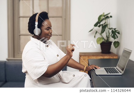 Grooving to the beat of success. Shot of a young businesswoman using headphones and a laptop in an office. 114326044