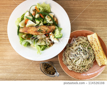 Pasta with mushrooms and a plate with a salad of vegetables and grilled salmon on a wooden background 114326108