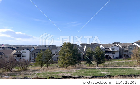 This image captures a serene suburban setting, showcasing a row of modern homes with distinct architectural styles, set against a backdrop of a clear blue sky and surrounded by natural greenery. 114326205