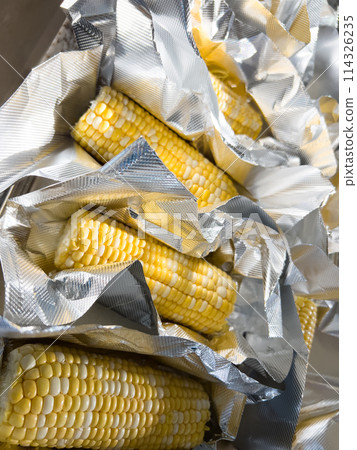 This image showcases fresh corn on the cob, neatly arranged in vacuum-sealed plastic packaging to preserve its freshness and flavor, ready for distribution or sale. 114326235
