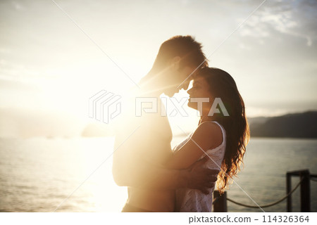Sunset, couple and touch face at ocean for holiday, vacation or travel together in summer on lens flare. Happy man, woman and romance at sea for connection, care or love on adventure by water outdoor 114326364