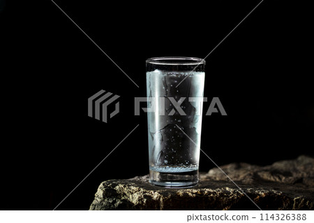 a glass of water with walls fogged up from the cold on a rock on a black background a glass of water with walls fogged up from the cold on a rock on a black background 114326388
