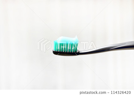 black toothbrush with toothpaste applied to it on a light background black toothbrush with toothpaste applied to it on a light background 114326420