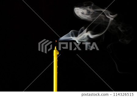 extinguished candle with a smoldering wick exudes smoke on a black background 114326515