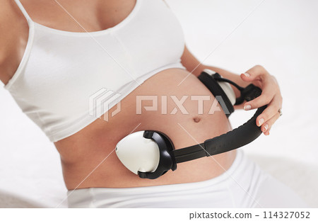 Woman, pregnant and headphones on stomach with music in studio for calming, parent or listening. Mother, audio and belly for soothing baby in womb for maternity bonding in home, streaming or relax Woman, pregnant and headphones on stomach with music in studio for calming, parent or listening. Mother, audio and belly for soothing baby in womb for maternity bonding in home, streaming or relax 114327052