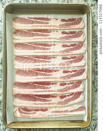 Neatly arranged raw bacon strips on a baking tray, prepared for cooking, capturing the fresh, uncooked look of this popular breakfast ingredient before it turns crispy and golden. Neatly arranged raw bacon strips on a baking tray, prepared for cooking, capturing the fresh, uncooked look of this popular breakfast ingredient before it turns crispy and golden. 114327066