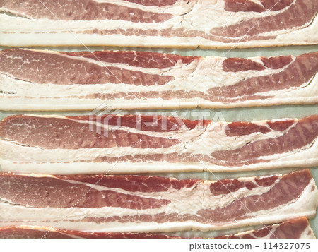 Neatly arranged raw bacon strips on a baking tray, prepared for cooking, capturing the fresh, uncooked look of this popular breakfast ingredient before it turns crispy and golden. Neatly arranged raw bacon strips on a baking tray, prepared for cooking, capturing the fresh, uncooked look of this popular breakfast ingredient before it turns crispy and golden. 114327075