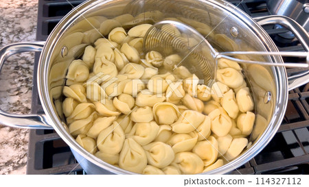 A large pot filled with boiling tortellini pasta showcases the preparation of this traditional Italian dish, with the pasta floating in water ready to be served, set on a modern gas stove. A large pot filled with boiling tortellini pasta showcases the preparation of this traditional Italian dish, with the pasta floating in water ready to be served, set on a modern gas stove. 114327112