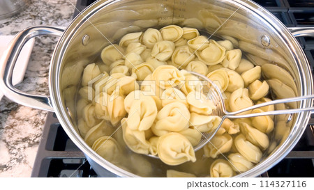 A large pot filled with boiling tortellini pasta showcases the preparation of this traditional Italian dish, with the pasta floating in water ready to be served, set on a modern gas stove. A large pot filled with boiling tortellini pasta showcases the preparation of this traditional Italian dish, with the pasta floating in water ready to be served, set on a modern gas stove. 114327116