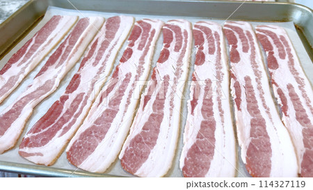 Neatly arranged raw bacon strips on a baking tray, prepared for cooking, capturing the fresh, uncooked look of this popular breakfast ingredient before it turns crispy and golden. Neatly arranged raw bacon strips on a baking tray, prepared for cooking, capturing the fresh, uncooked look of this popular breakfast ingredient before it turns crispy and golden. 114327119