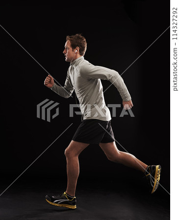 Man, music or fitness in studio with running for exercise, marathon or workout with earphones. Athlete, person or cardio for healthy body, wellness or training with radio or audio on black background 114327292