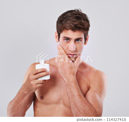 Young man, portrait and aftershave with cosmetics for skincare or lotion on a gray studio background. Face of handsome male person or model with beauty creme or container for hygiene on mockup space 114327418