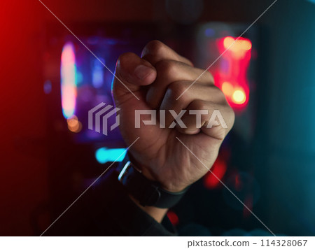 Hand, neon and fist for success in esports, online and gaming with person at home in dark room. Influencer, winner and gamer with playing for internet event, video game and live streaming in bedroom 114328067