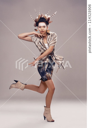 Woman, dancer and portrait for culture fashion in studio, feathers and tribal make up in trendy clothes. Native american, model and face in indigenous cosmetics and accessories on grey background 114328906