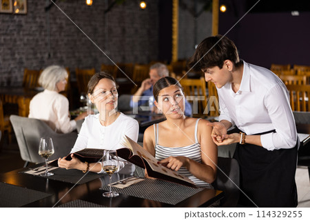 Young male waiter taking order from two women in restaurant 114329255