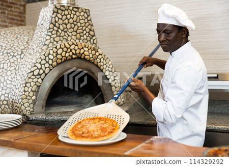 Portrait of happy chef getting ready pizza out of oven in kitchen 114329292