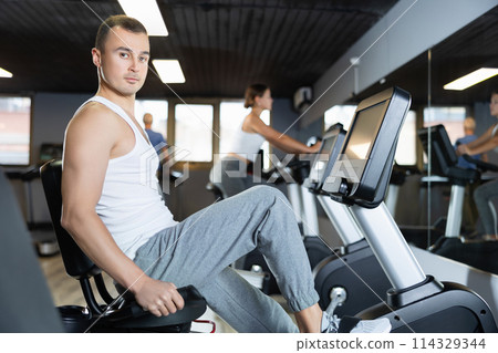 Portrait of concentrated man doing cardio training, cycling on stationary bike in gym. Sport and fitness concept 114329344