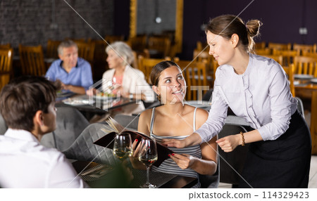 Waitress recommending dishes from menu to young couple 114329423