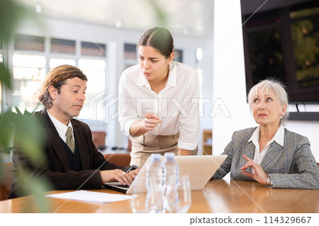three positive office workers are sitting at table animatedly and actively discussing current work 114329667