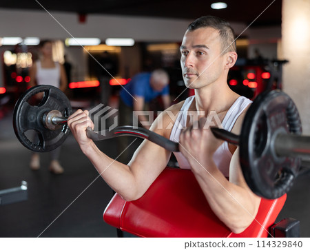 Sporty man performing set of exercises with barbell during intense workout 114329840