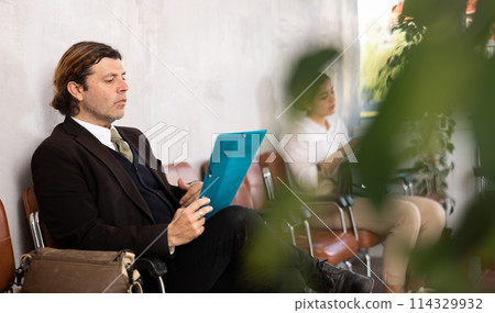 Serious-minded male candidate siting on chair and waiting for job interview in hallway Serious-minded male candidate siting on chair and waiting for job interview in hallway 114329932
