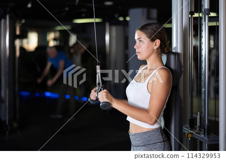 Athletic girl work out muscles of arms and shoulders on rope loop simulator in gym of fitness club 114329953