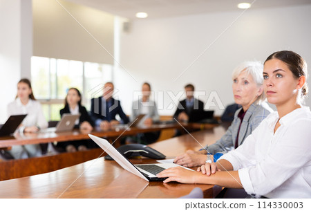 Young woman secretary typing on laptop during conference 114330003