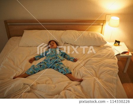 Boy, bed and rest for night, sleeping and tired with fatigue and peace. Child, dreaming and exhausted with pyjamas, dark and bedroom with lamp for serene childhood at home or house for calm kid 114330226