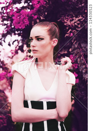 Fashion, nature and young woman with beauty, elegant and trendy dress outfit with confidence. Attractive, makeup and female person with classy and edgy style by flowers, plants or bush in garden. 114330523
