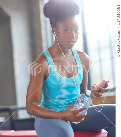 Portrait, gym and black woman listening to music, water bottle and fitness with progress and healthy. Face, African person and athlete with hydration and song for exercise motivation and relaxing 114330561