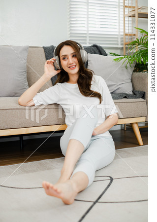 Young woman enjoys her favorite tunes, lounging comfortably on the floor at home with a stylish pair of headphones. Young woman enjoys her favorite tunes, lounging comfortably on the floor at home with a stylish pair of headphones. 114331077