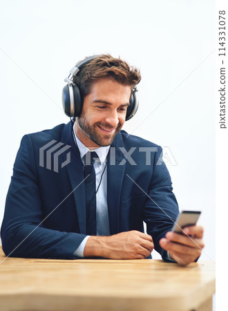 Headphones, office and businessman with mobile phone for social media, browsing internet or streaming music. Smile, smartphone and male person listening to radio, audio podcast or online ted talk Headphones, office and businessman with mobile phone for social media, browsing internet or streaming music. Smile, smartphone and male person listening to radio, audio podcast or online ted talk 114331078