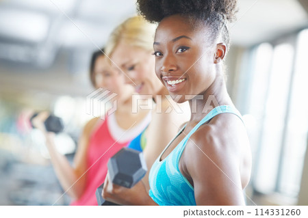 African athlete, dumbbell and portrait with smile in gym for workout, class and muscle growth. Woman, weight and happiness for exercise in fitness center for training, sport and strength development African athlete, dumbbell and portrait with smile in gym for workout, class and muscle growth. Woman, weight and happiness for exercise in fitness center for training, sport and strength development 114331260