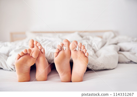Feet, bed and couple in blanket with sleep for relax on honeymoon with getaway for togetherness and love in room. Toes, rest and intimacy vacation with duvet in house on weekend with comfort 114331267
