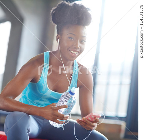 Fitness app, headphones and portrait of black woman in gym with water, phone or online subscription. Health, wellness and girl checking music playlist on smartphone with bottle, break and sports club 114331379