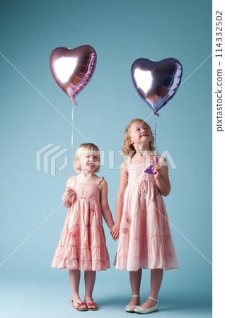 Children, holding hands and sister with heart balloon in studio on blue background for family or party. Birthday, celebration event or happy with smile of girl kids on color backdrop together 114332502
