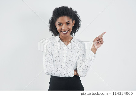 Pointing, happy and portrait business black woman in studio for promotion on white background. Advertising, professional and isolated person with hand gesture for announcement, news and information 114334060