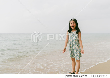Portrait an Asian happy child girl standing on a beach, shouting happily, bright light image with space. Portrait an Asian happy child girl standing on a beach, shouting happily, bright light image with space. 114334983