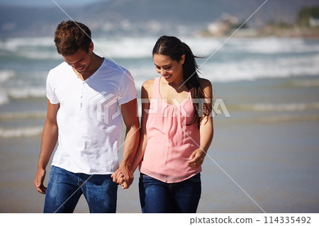 Happy couple, holding hands and walking on beach with support, love or care on outdoor holiday in nature. Young man and woman with smile for honeymoon, relationship or weekend together by ocean coast 114335492