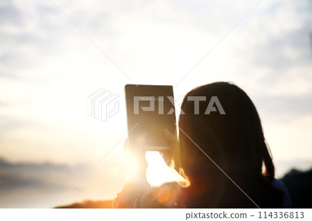 Christian woman holding high holy bible with sunset sky and bright light sun background, Christian faith concept 114336813