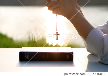 Christian praying, meditating and worshiping with hands together, brightly lit cross and Bible book background Christian praying, meditating and worshiping with hands together, brightly lit cross and Bible book background 114336818
