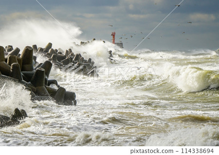 Stormy weather, big waves crashing against the concrete breakwaters of the port with high splashes 114338694