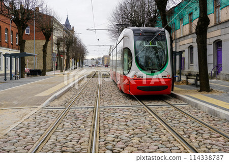 A modern low-floor tram car at a newly built stop platform and paved intermediate track surface 114338787
