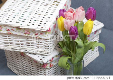 Bouquet of tulips of different colors on a gray background. Near wicker boxes. 114338971