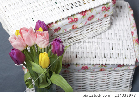 Bouquet of tulips of different colors on a gray background. Near wicker boxes. Bouquet of tulips of different colors on a gray background. Near wicker boxes. 114338978